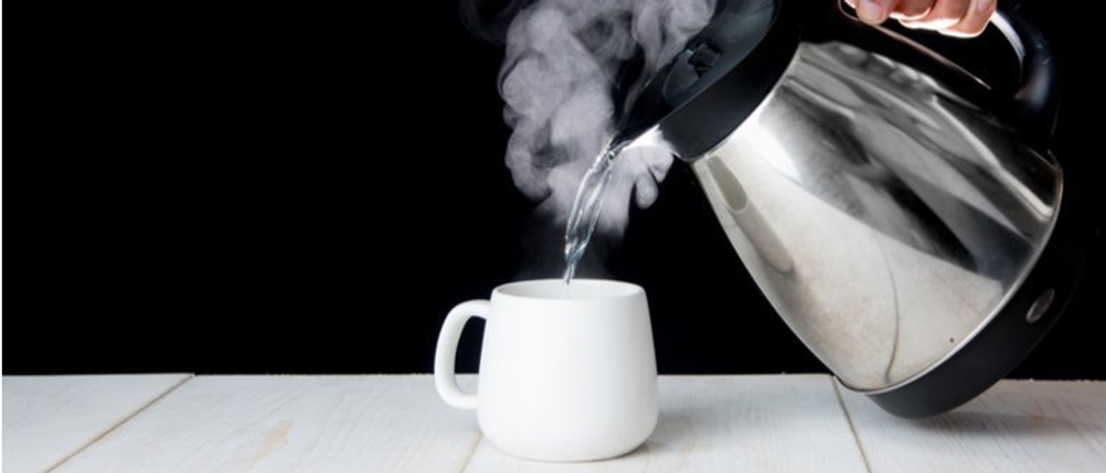Dampfendes Wasser wird aus einem Wasserkocher in eine Tasse gegossen.