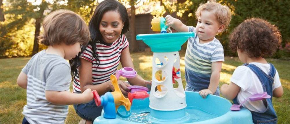 Wasserspieltisch im Test: Eine Frau, die mit drei Kindern an einem Wasserspieltisch spielt.