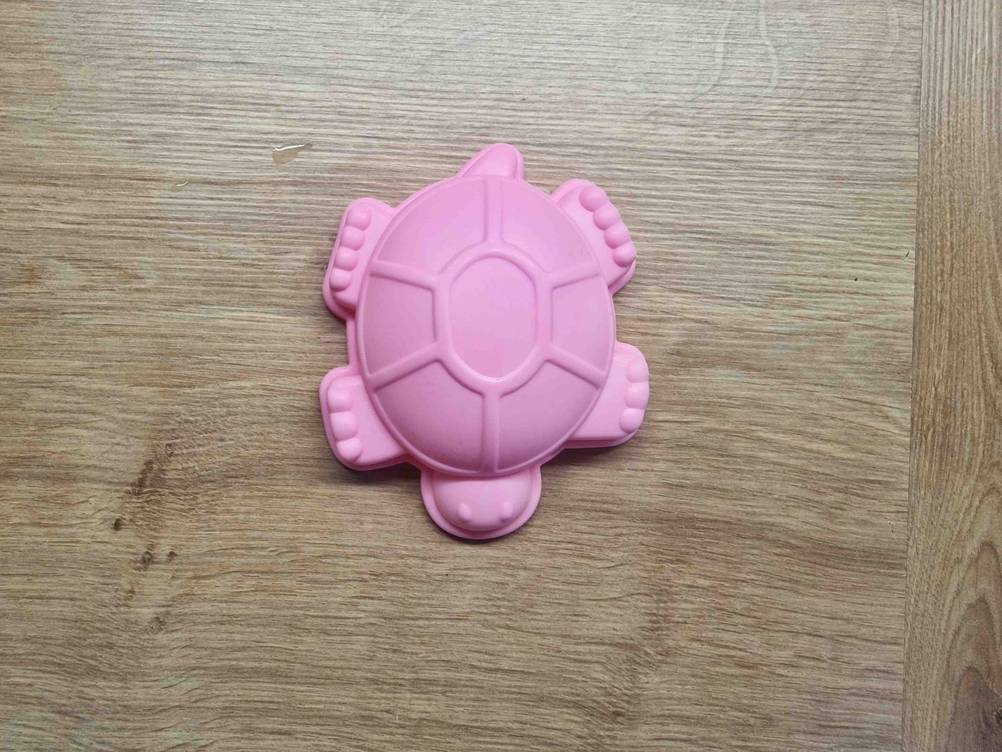 Ein getestetes Wasserspielzeug in Form einer Schildkröte auf einer Holzfläche von oben.
