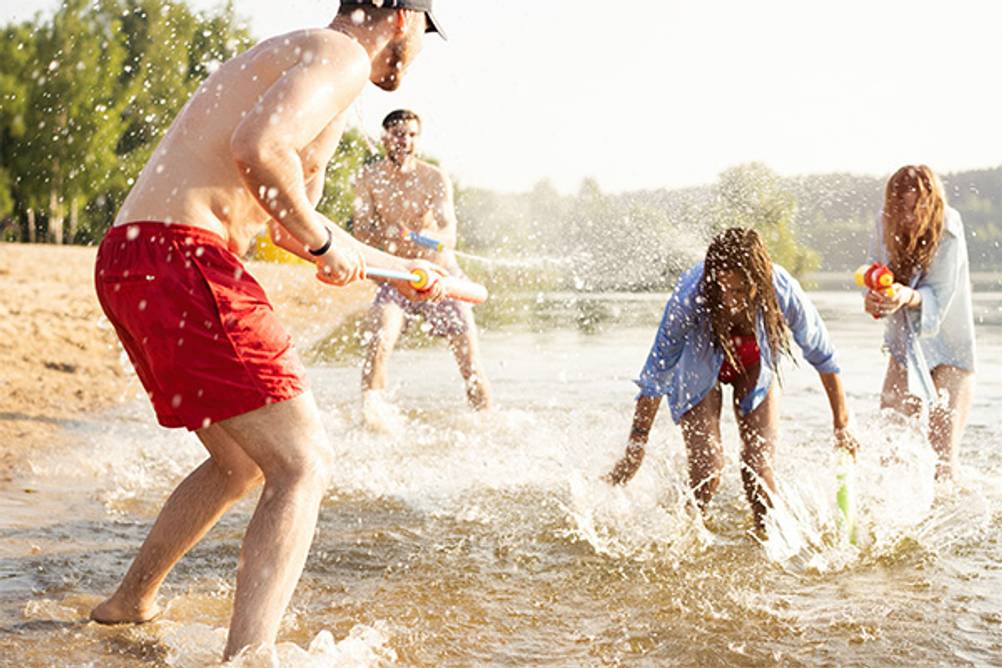 Wasserspritzen im Test: Vier junge Leute, die sich mit Wasserspritzen und Wasserpistolen eine Wasserschlacht liefern.