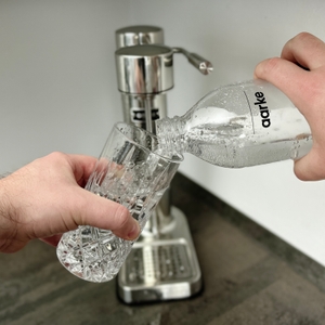 Sprudelwasser aus einer Aarke-Flasche wird in ein Glas eingeschenkt. Der Aarke Carbonator 3 steht im Hintergrund.