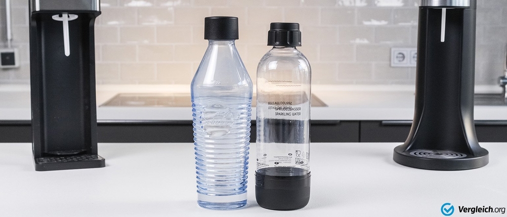 Eine Glasflasche steht zwischen zwei Wassersprudlern neben einer Kunststofflasche