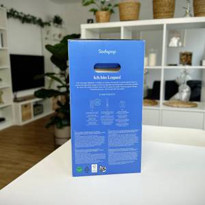 Die Verpackungsseite des Sodapop Logan mit Produktinformationen und Nutzungshinweisen. Im Hintergrund ist eine moderne Wohnküche.