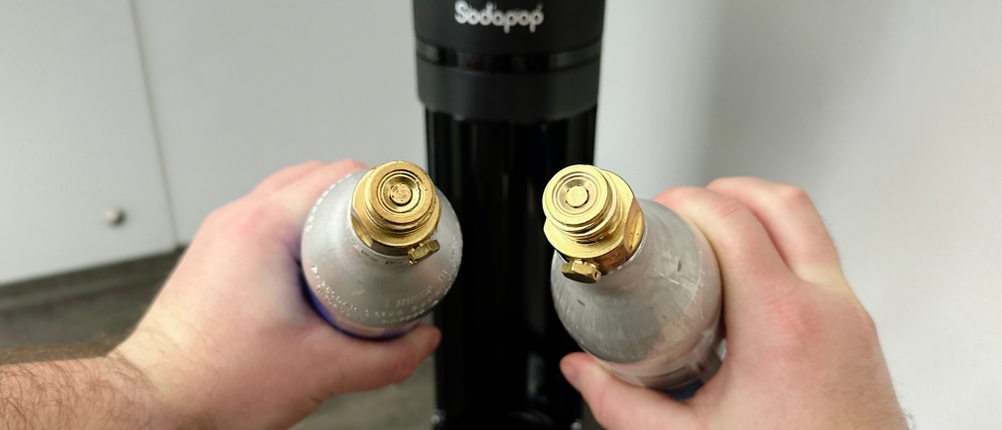 Zwei verschiedene CO₂-Zylinder werden vor dem Sodapop Logan gehalten. Beide Zylinder haben eine Schraubverbindung.