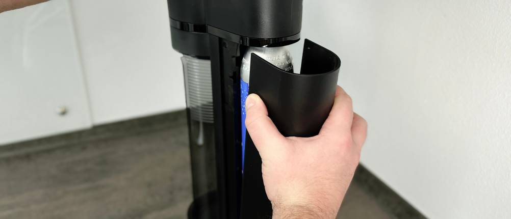 Ein CO₂-Zylinder wird in den Sodapop Logan eingesetzt. Die schwarze Abdeckung wird gleichzeitig geöffnet.