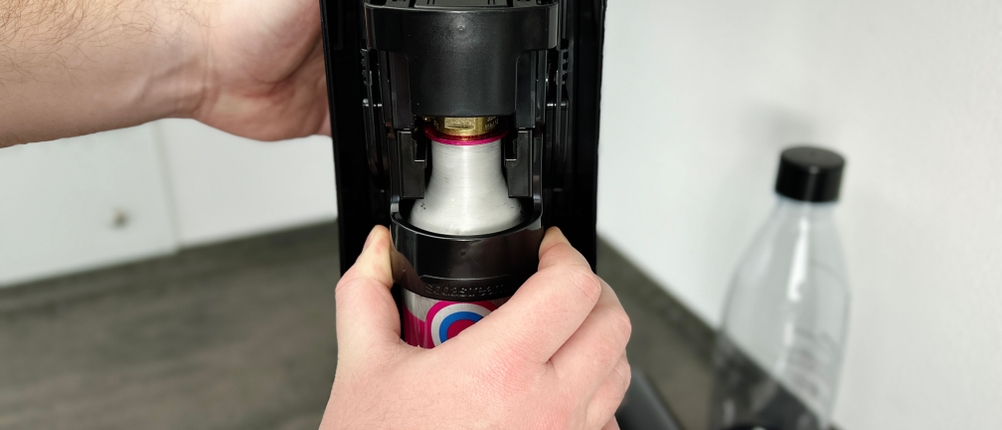 Ein CO₂-Zylinder wird in den Sodastream Terra eingesetzt. Die Hände halten das Gerät stabil, während der Zylinder in die Halterung gedrückt wird.