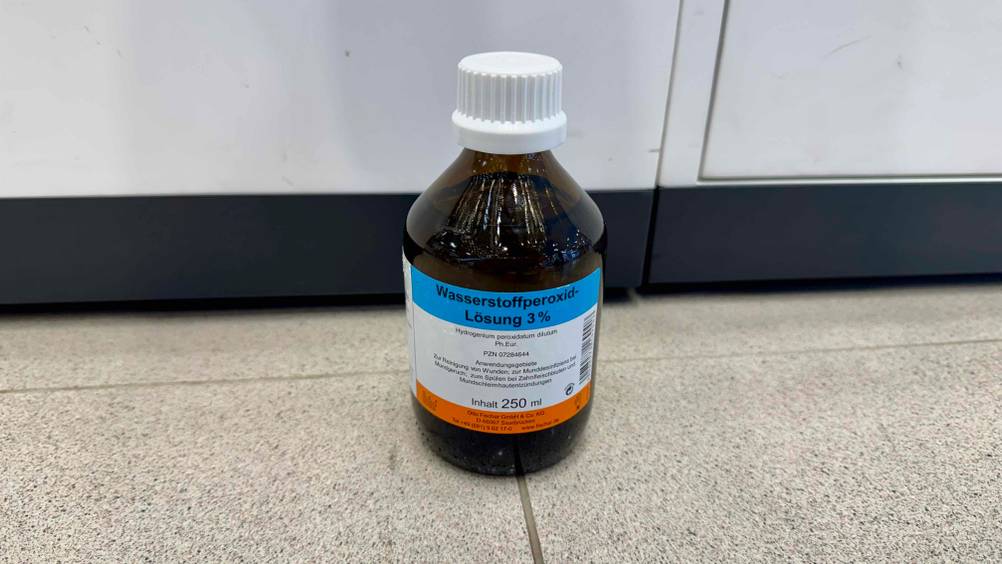 Das Wasserstoffperoxid 3 Prozent im Test vor einem Schrank auf dem Boden stehend.