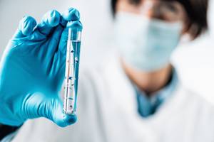 Wassertest-Test: Eine Person mit blauen Handschuhen aus Gummi hält ein Reagenzglas in der Hand.