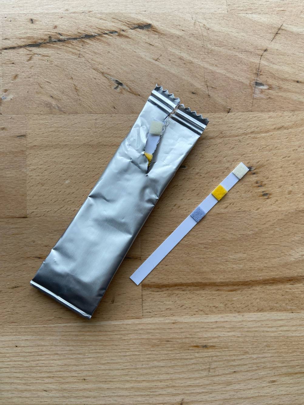 Auf einer Holzfläche liegt einer der getesteten Wasserteststreifen neben der silbernen Verpackung.