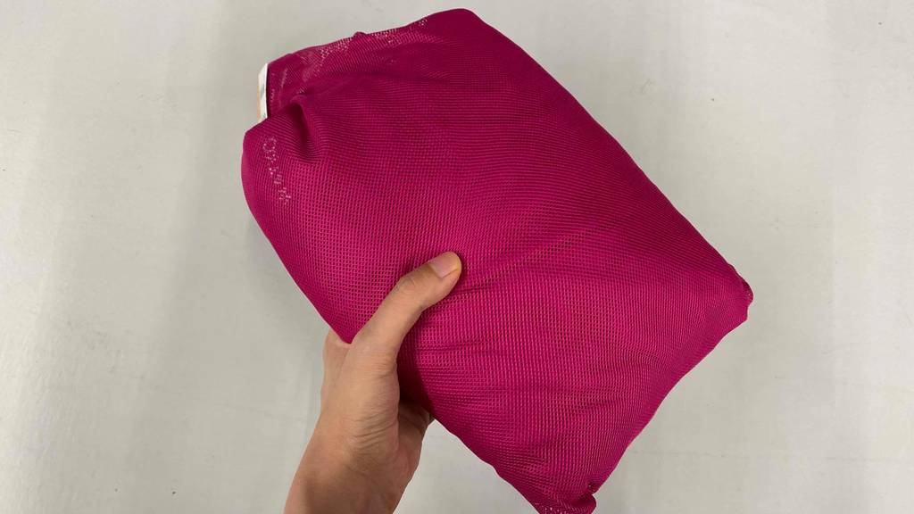 Hand hält rosa, zusammengefalteten und getesteten Damen-Bademantel vor hellem Hintergrund.
