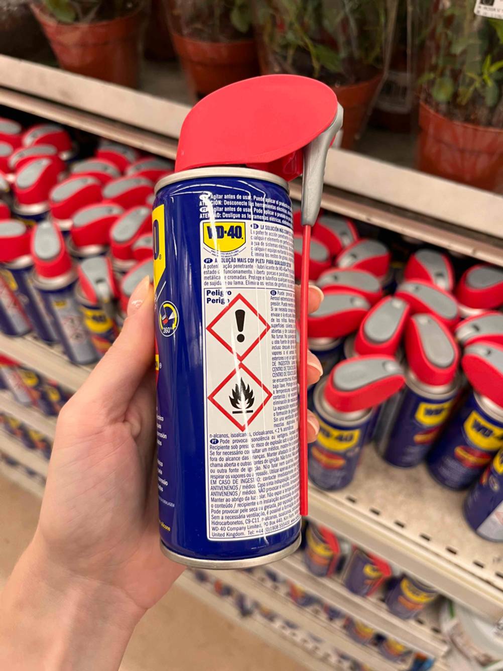 Hand hält ein WD-40-Druckluftspray im Test, mit Blick auf die Beschreibung und den ergonomischen, roten Sprühkopf inklusive Verlängerung, vor einem Verkaufsregal.