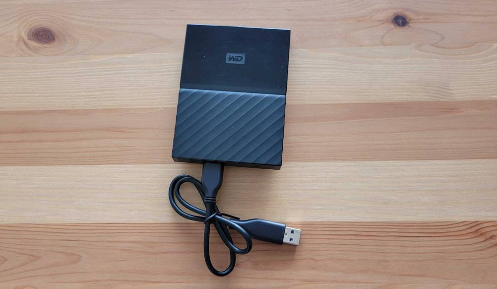 Eine externe SSD Festplatte mit 1 TB liegt mit USB-Kabel auf einem Holzboden.