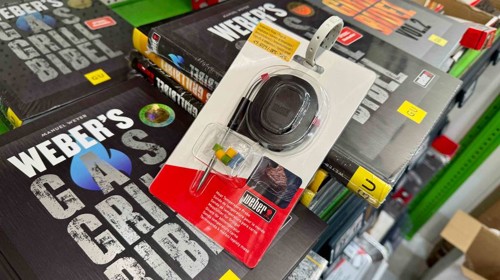 Ein im Blister verpacktes Weber-Grillthermometer lehnt zum testen an mehrere Bücher.