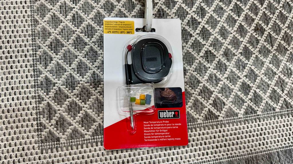 Ein verpacktes Weber-Grillthermometer liegt zum testen auf einem grauen Teppich.