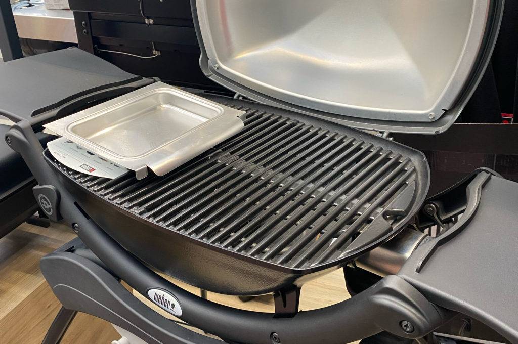Grill getestet: grauer Weber-Standgrill inklusive geöffnetem Deckel, Grillrost und Seitenablagen steht in einem Verkaufsbereich.