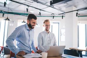 Webhosting-getestet: Zwei Männer im Hemd stehen lächelnd vor einem Laptop.