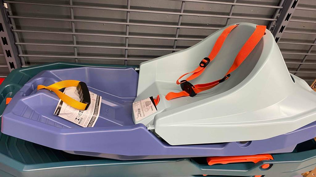 Seitenansicht eines Babyschlittens im Test: zweifarbiger Schlitten (hell- und dunkelgrau) steht inklusive Gurtsystem in einem Verkaufsregal.