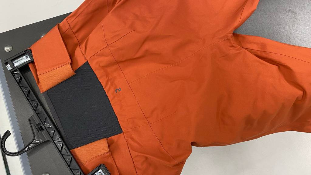 Herren-Skihose-Test: orange Skihose mit hinterem, schwarzem Gummizug-Einsatz liegt auf dem Boden.