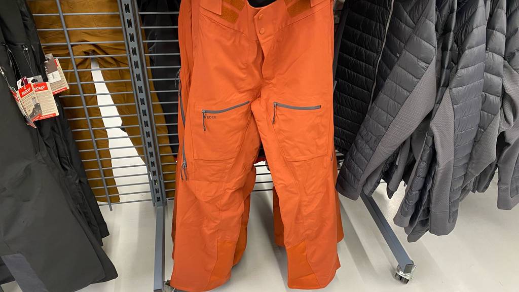 Herren-Skihose im Test: orange Skihose inmitten von anderer Skibekleidung an einem Verkaufsstand.