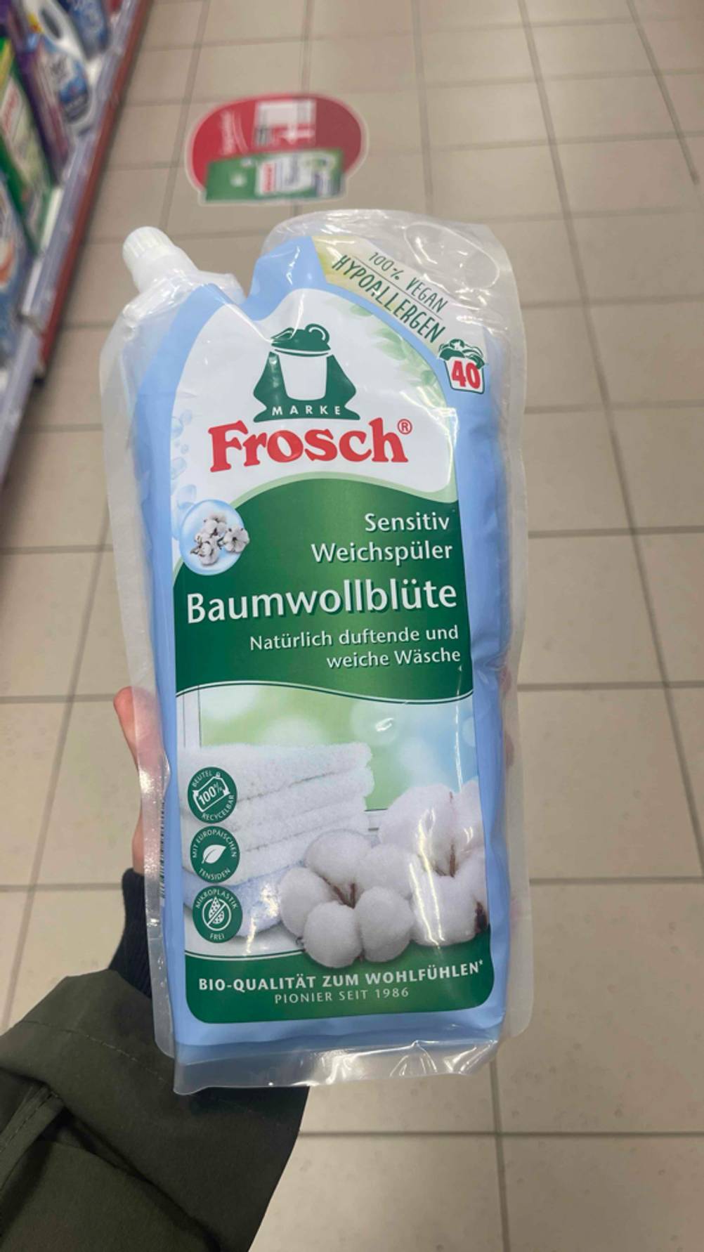 Eine Hand hält den getesteten veganen Weichspüler im Nachfüllpack über einem weißen Fliesenboden.