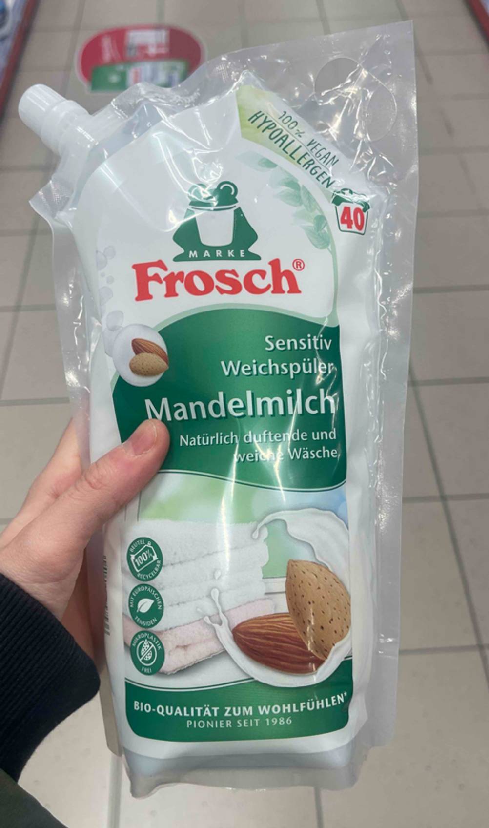 Eine Hand hält einen Nachfüllbeutel mit veganem Weichspüler im Test über einem weißen Fliesenboden.