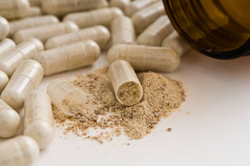 Weidenrinde-Kapseln-Test: Mehrere geschlossene und offene Kapseln mit hellbraunem Pulver liegen neben einer offenen Dose. 
