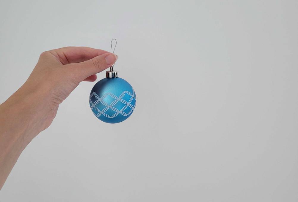 Eine Hand hält eine blaue Weihnachtskugel im Test vor eine helle Wand.