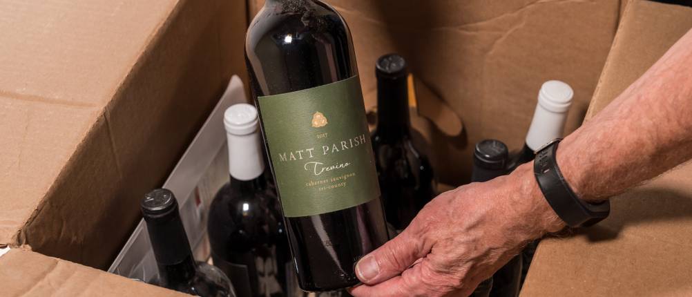 Wein kaufen Test: Ein Mann holt eine Weinflasche aus einem Karton mit mehreren Weinflaschen.