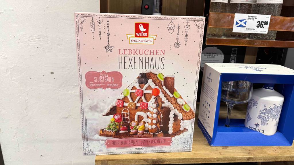 Die Verpackung mit dem getesteten Lebkuchenhaus zum Selbstbauen steht neben einem Dry-Gin-Glas-Set auf einem Regal im Verkaufsbereich.