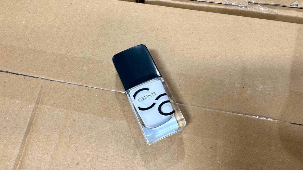 Auf einem Karton liegt eine Flasche des weißen Nagellacks.