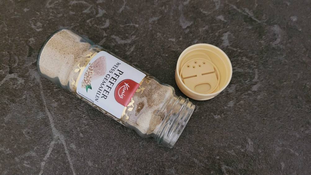 Auf dem Küchentisch befindet sich getesteter weißer Pfeffer in einem Kuntstoffbehälter. 