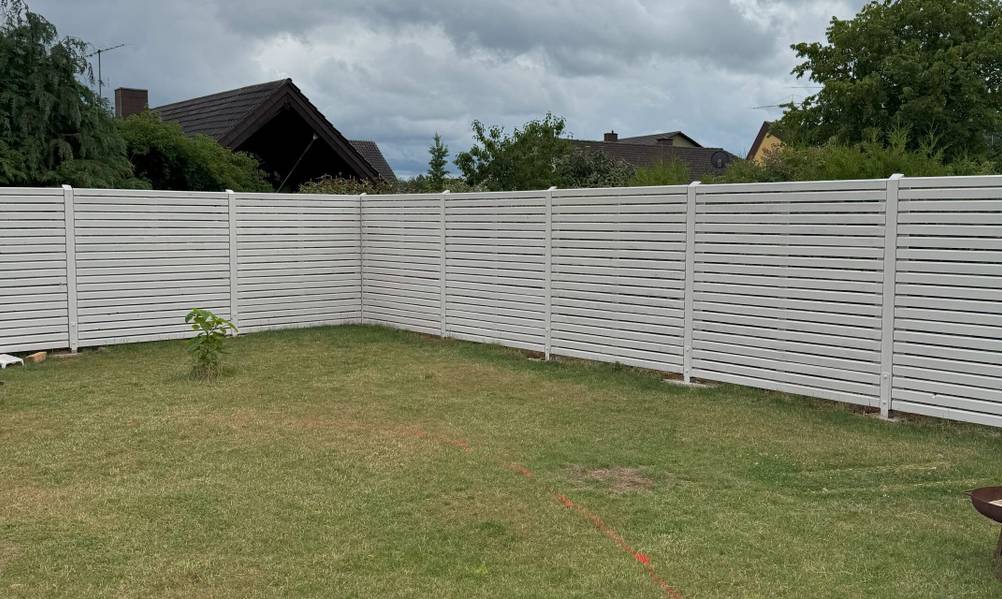 Ein weißer Rhombus-Zaun umgibt einen Garten.