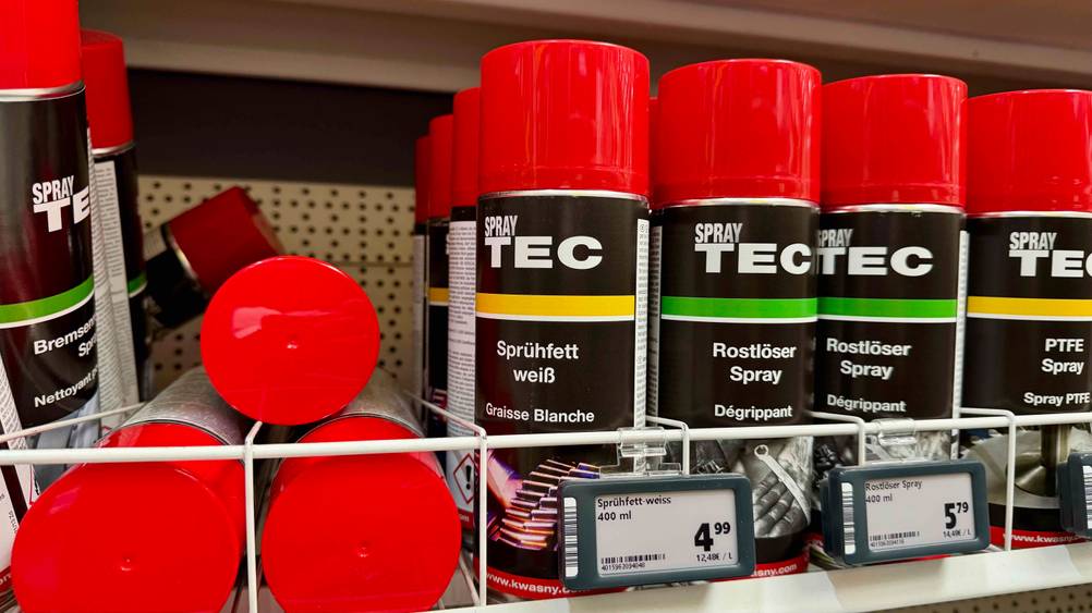 Mehrere Dosen des Weißes Sprühfett im Test in einem Verkaufsregal neben anderen Produkten.