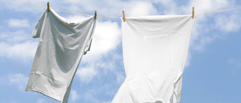 Test von weißen T-Shirts für Herren: Zwei weiße T-Shirts hängen an einer Wäscheleine und im Hintergrund ist der leicht bewölkte blaue Himmel zu sehen.
