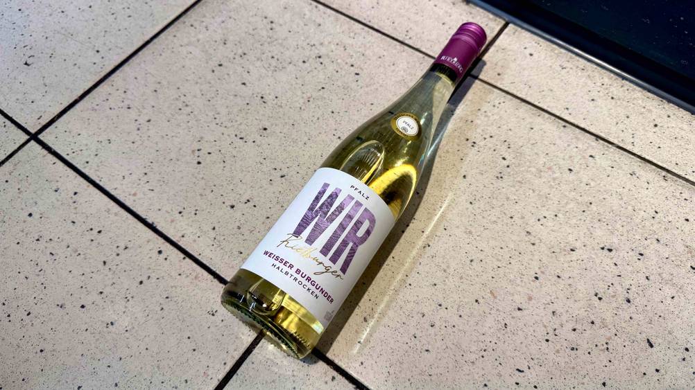 Auf einem Fließenboden liegt eine Flasche des Weißwein (halbtrocken) im Test.