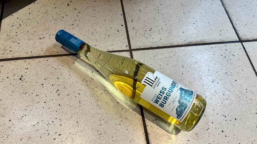 Auf eine Fließenboden liegt eine Flasche des Weißwein (trocken) im Test.