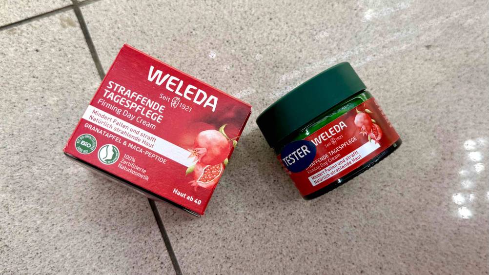 Neben der Verpackung liegt ein Tiegel Weleda-Gesichtscreme auf einem Fließenboden.