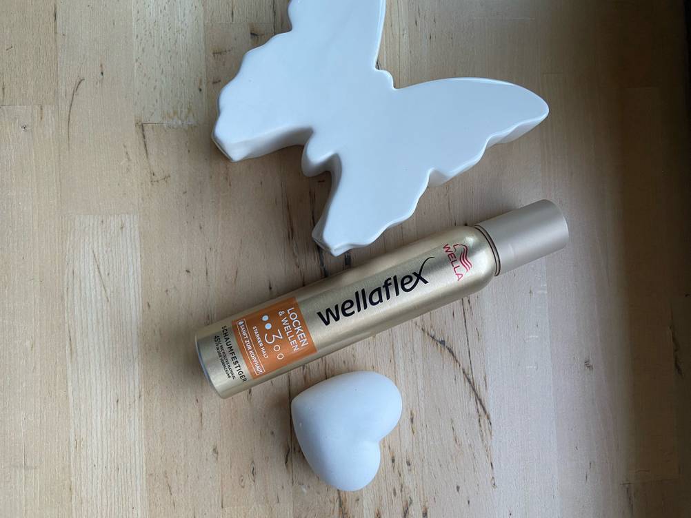 Im Test: Eine Flasche Wella-Schaumfestiger liegt zwischen einem Schmetterlings- und einem Herzdekoteil.