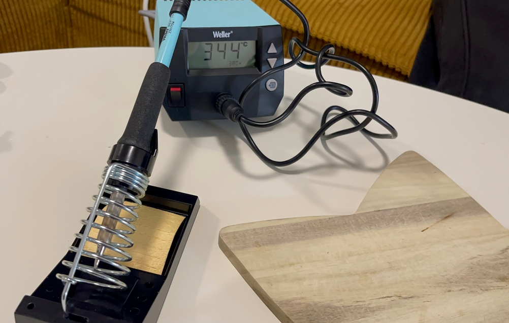 Das Weller WE 1010 Lötgerät ist in Betrieb und zeigt auf dem Display eine Temperatur von 344 °C an. Der Lötkolben liegt in der Halterung mit Metallspirale und Reinigungsfläche aus Messing.