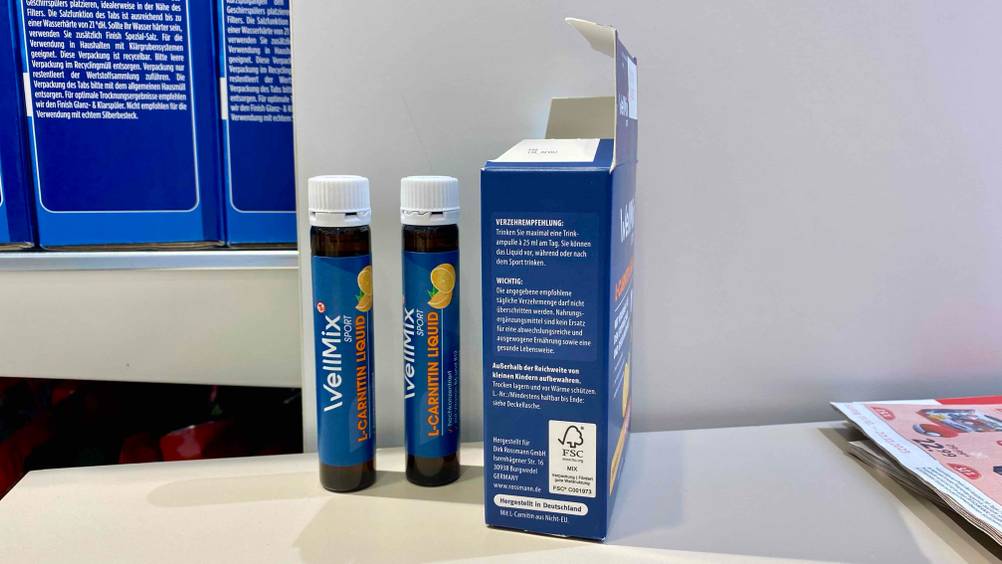 Zwei Röhrchen L-Carnitin stehen zum testen neben der geöffneten Orginalverpackung, auf der die Verzehrempfehlung angegeben ist.