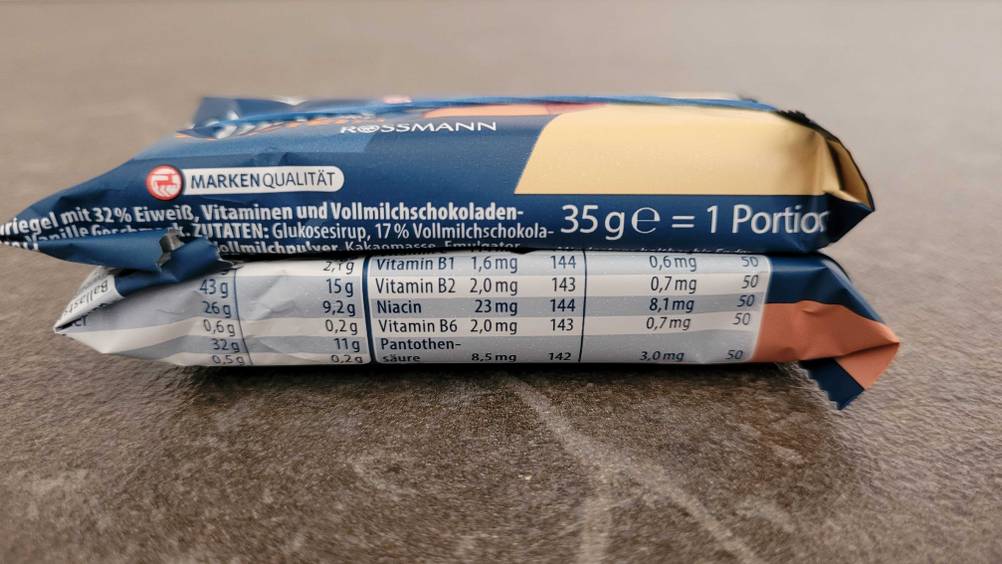 Proteinriegel getestet: Zwei aufeinander gestapelte Proteinriegel von der Seite auf einer grauen Fläche.