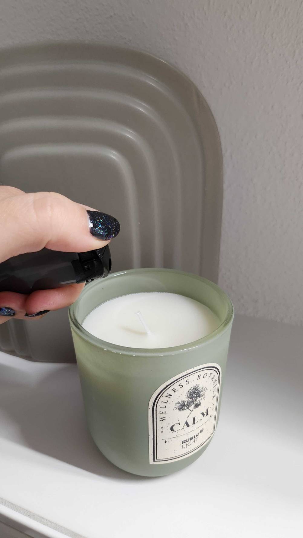 Eine Hand hält ein Feuerzeug über einer getesteten Kerze im Glas.