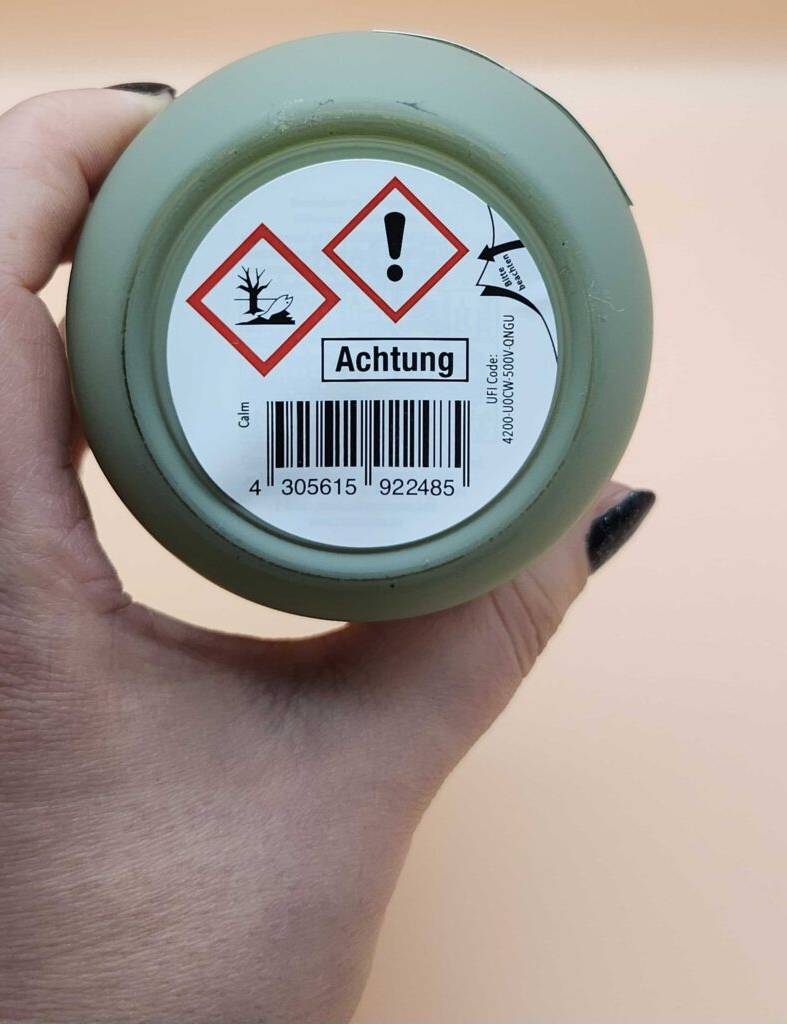 Eine Hand hält den Deckel inklusive Etikett mit Warnhinweis einer Kerze im Glas, die getestet wurde.