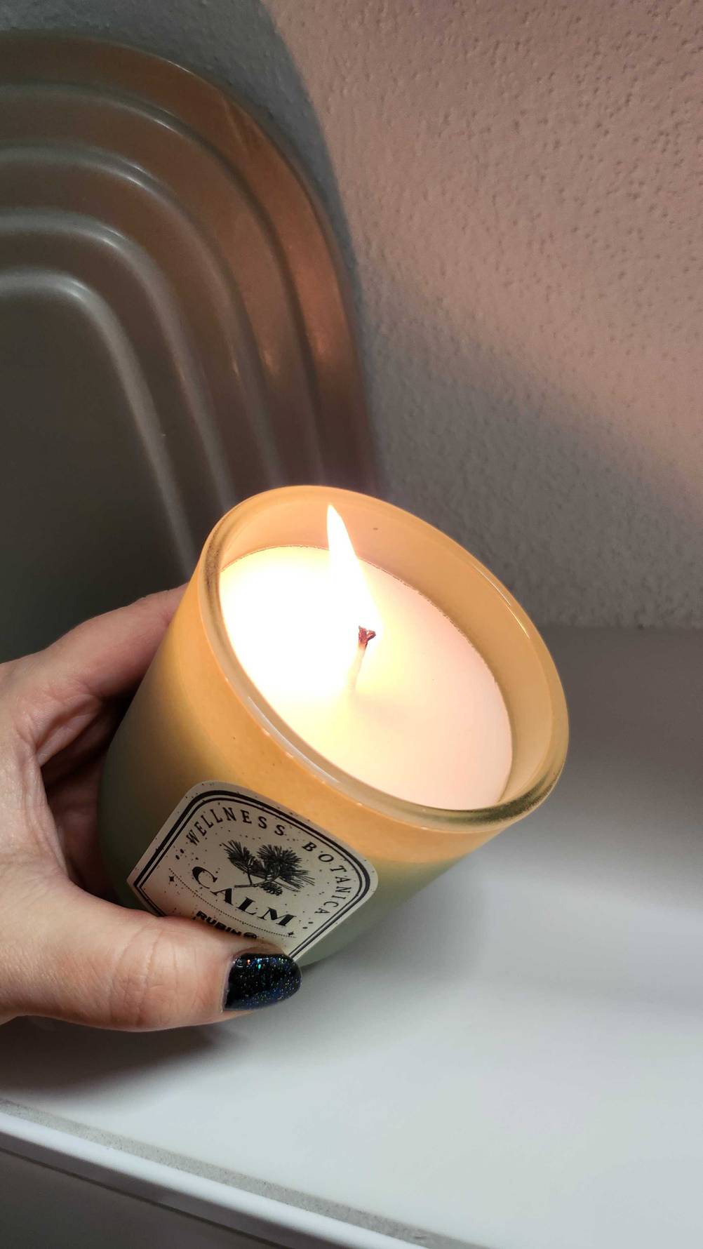 Eine Hand hält eine brennende getestete Kerze im Glas schräg.