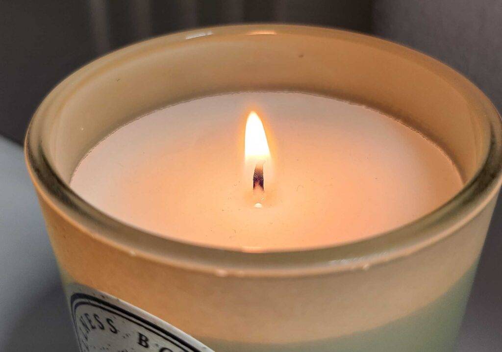 Die Detailansicht des brennenden Dochtes einer getesteten Kerze im Glas.