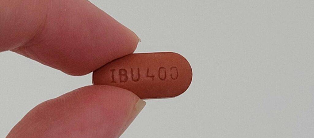 Hand hält eine braune IBU-400 Kopfschmerztablette im Test vor einem weißen Hintergrund.