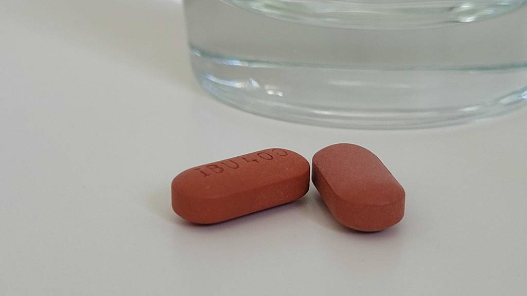 Zwei braune IBU-400 Kopfschmerztabletten im Test liegen vor einem Wasserglas auf einer weißen Oberfläche.