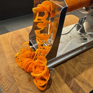 Karottenspiralen fallen vom Spiralschneider auf ein Brett.