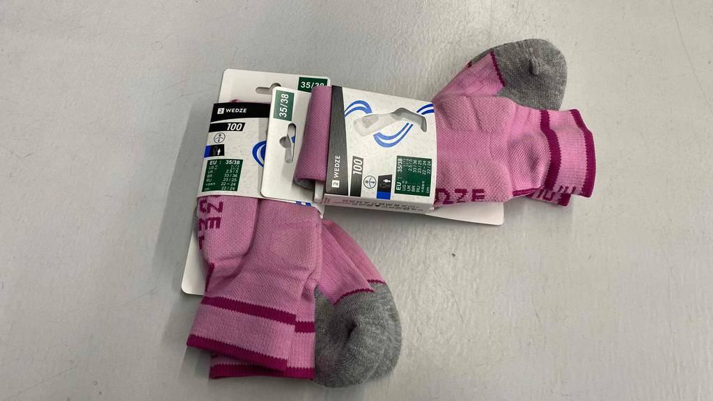 Zwei Paar rosa Wende-Skisocken im Test mit grauer Sohlen- und Zehen-Verstärkung liegen in ihren Verpackungen auf einer hellen Fläche.