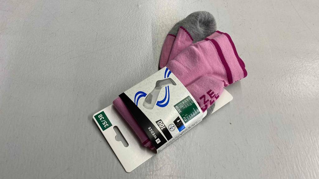 Getestete rosa Wende-Skisocken mit grauer Sohlen-Verstärkung liegen in ihrer Verpackung auf hellem Untergrund.